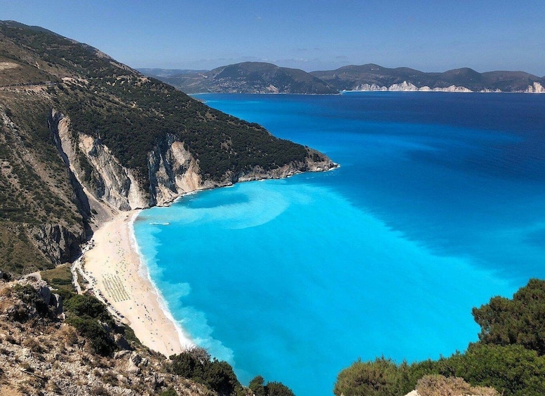 A coastal landscape with a clear blue sea, a sandy beach, and a mountainous backdrop. 4