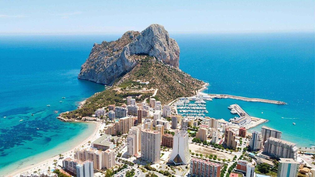 A coastal cityscape with a prominent rocky island, marina, and high-rise buildings. 5
