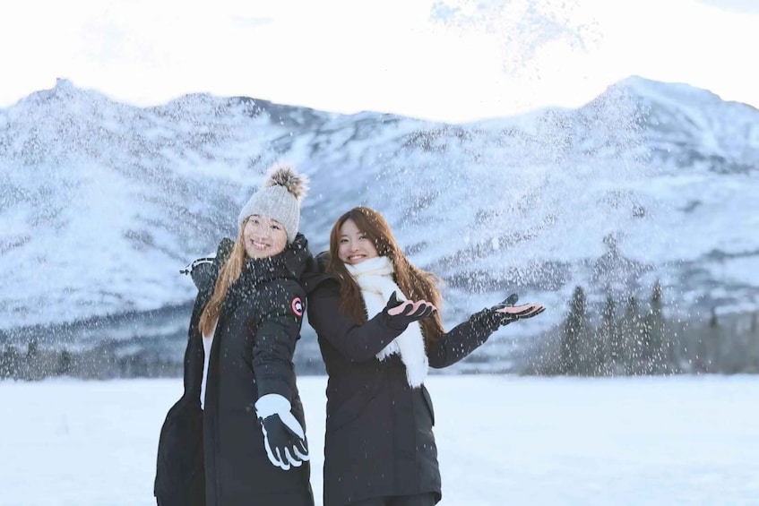 Two people in winter clothing throwing snow in a snowy landscape with mountains in the background. 2