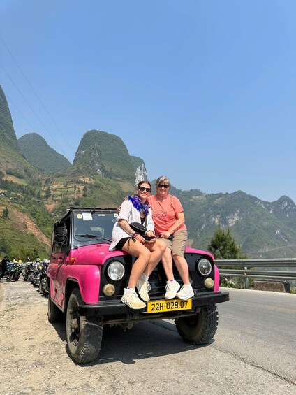 Two people sitting on a pink off-road vehicle with a mountainous landscape in the background. 3