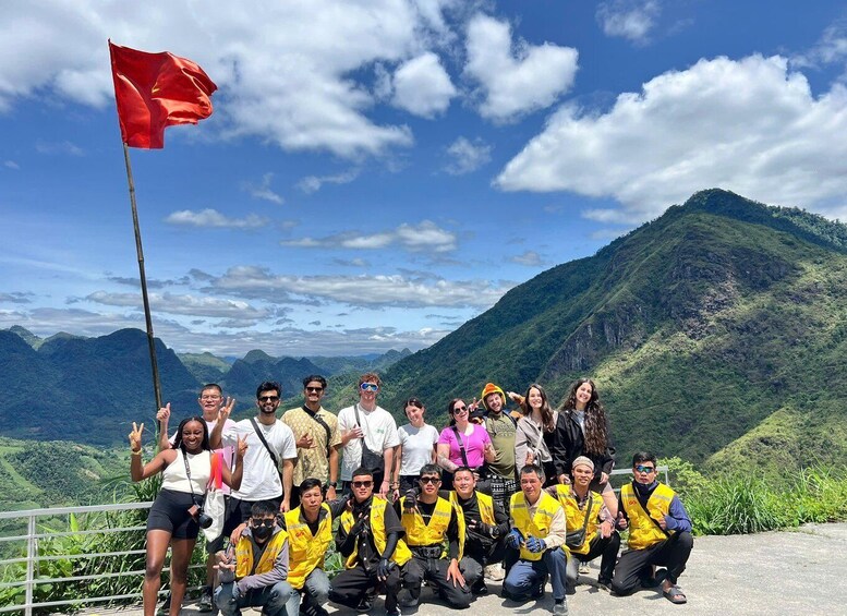 A group of people posing in front of a mountainous landscape with a red flag. 2