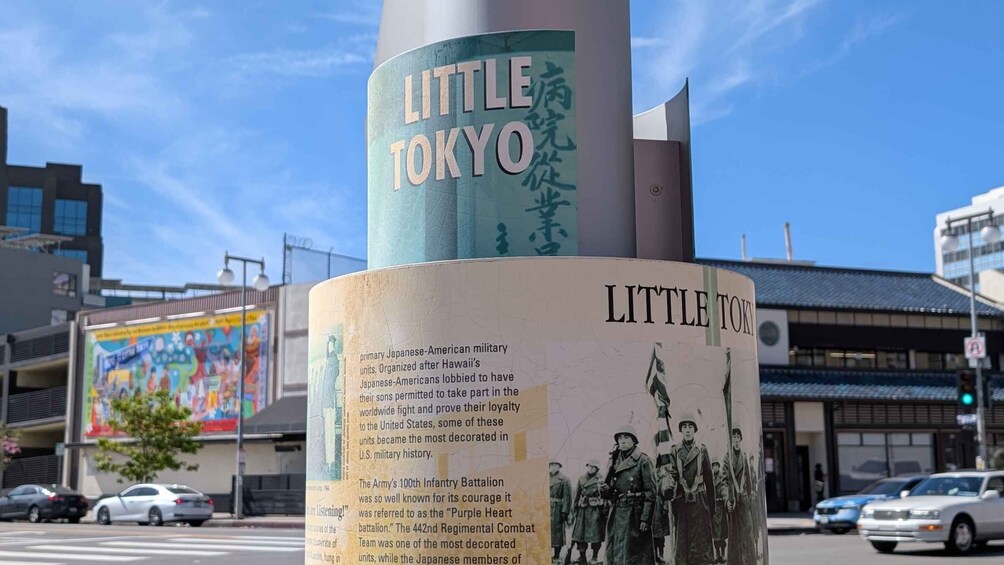 Ett monument med text och historiska fotografier, placerat mot en stadsbild med byggnader och bilar. 1