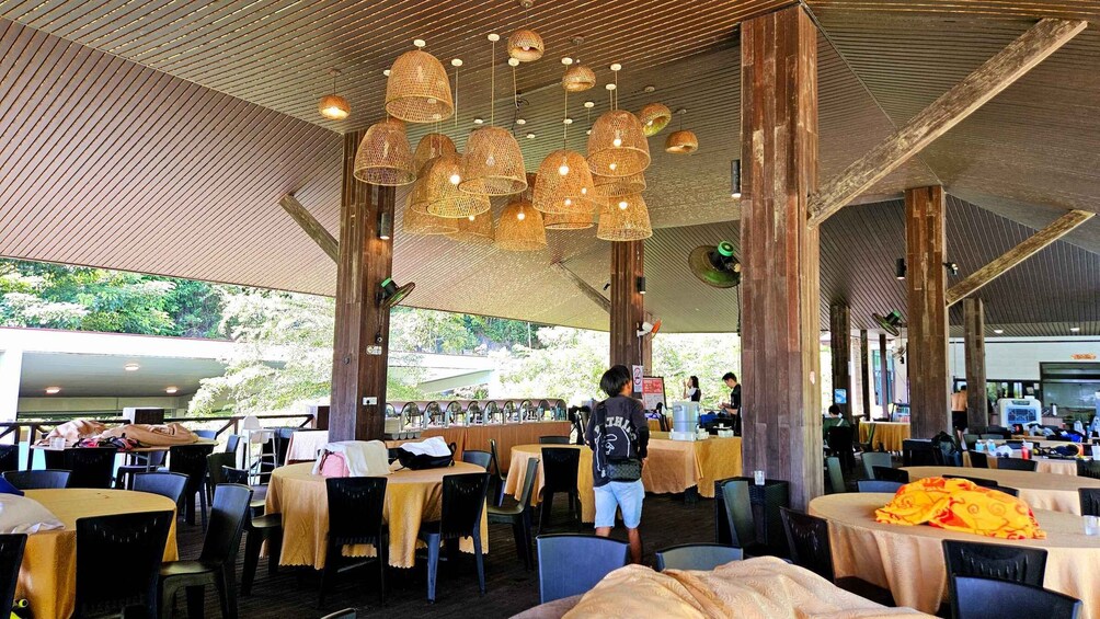 An outdoor restaurant with round tables, wicker hanging lights, and a view of greenery. 4