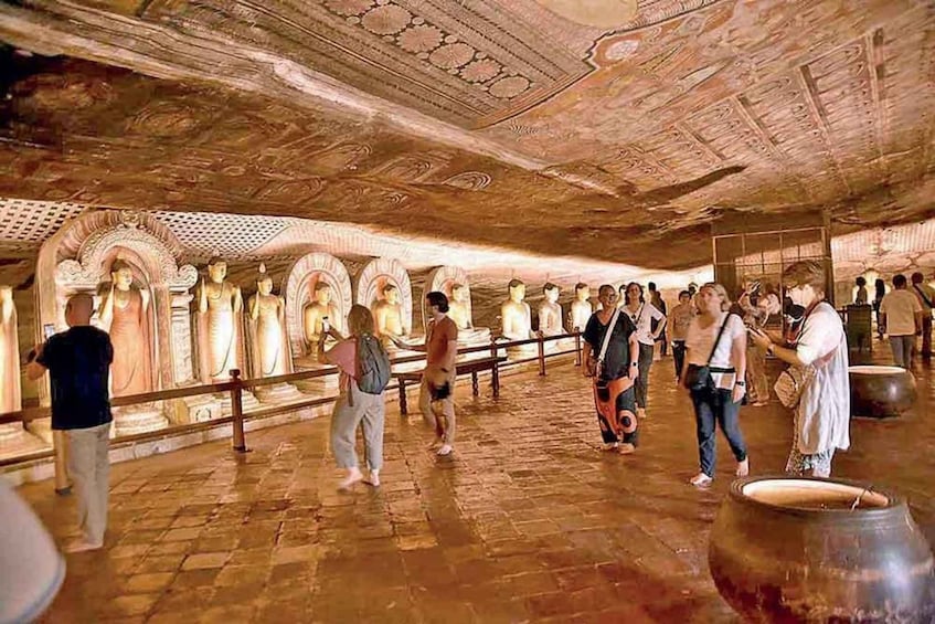 A cave temple with rows of statues and visitors. 1