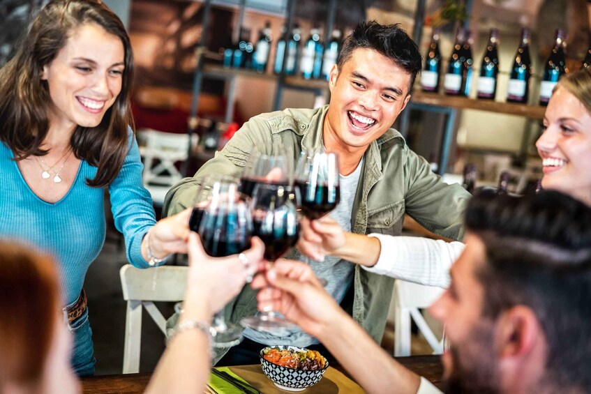 People toasting with wine glasses at a bar with shelves of bottles in the background. 2