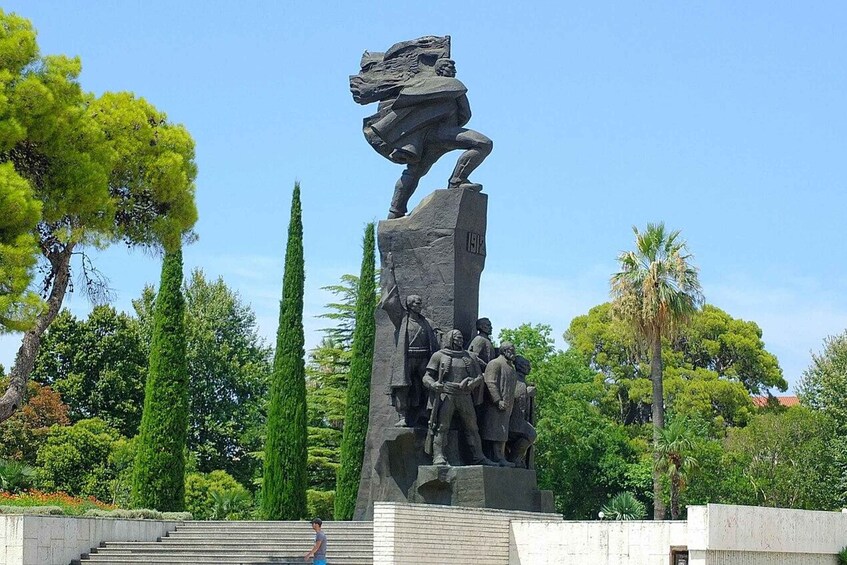 A statue of a horseman with a flag, surrounded by trees and a clear sky. 5