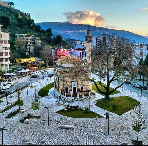A city square with a historic tower, modern buildings, and a mountain in the background. 1
