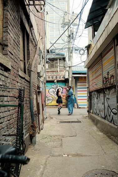 A narrow alley with brick walls, a colorful mural, and a closed shop with a metal shutter. 2