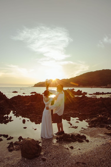 A couple standing on a rocky beach with the sun setting in the background. 3