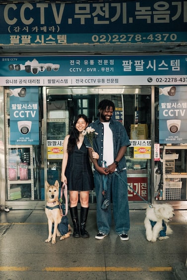 A storefront with CCTV and security service advertisements, a woman and a man standing in front, and two dogs. 5