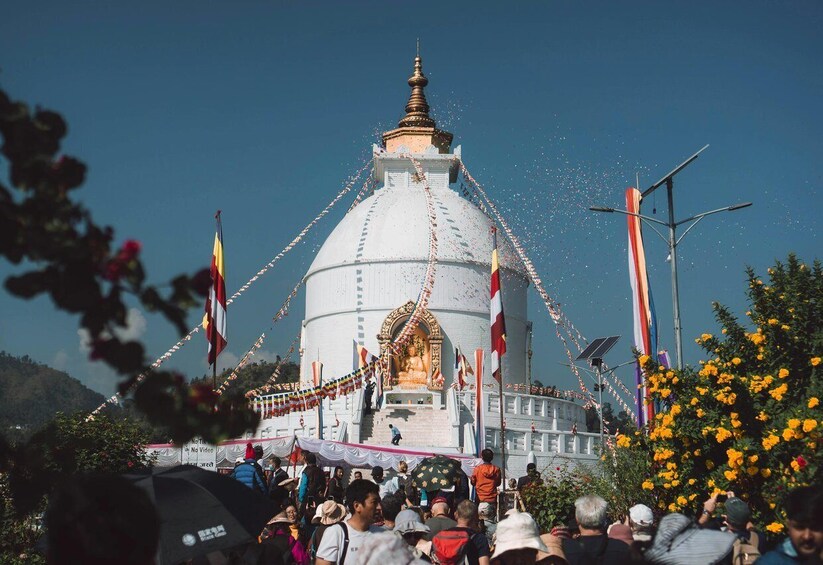 A large white stupa with a golden spire, surrounded by flags and a crowd of people. 2