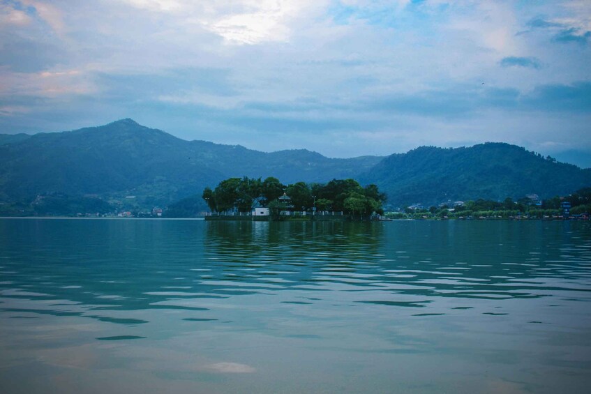 A calm lake with a small island in the center, surrounded by mountains and a cloudy sky. 5