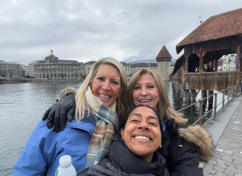 Tres personas posando junto a un río, con edificios históricos y una torre al fondo. 1