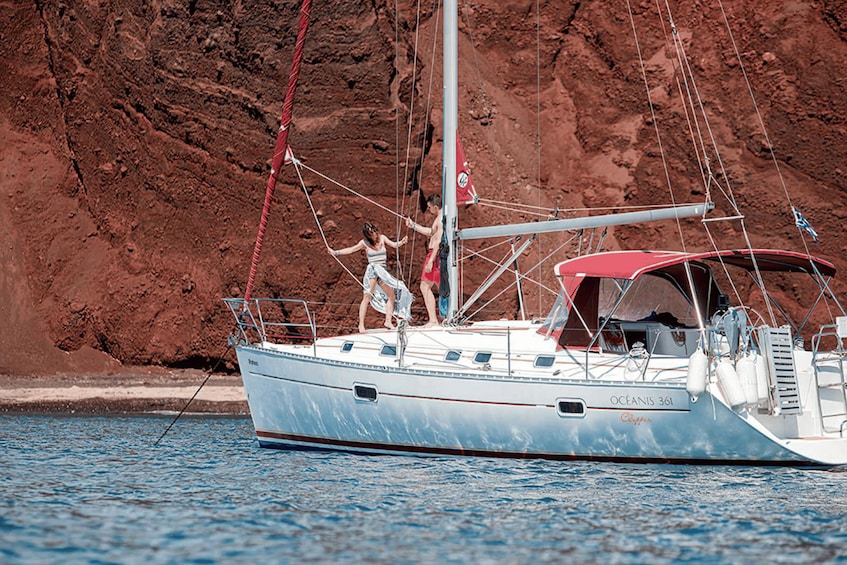 A sailboat named 'OCEANIS 361' with a red canopy, anchored near a rocky coastline. 2