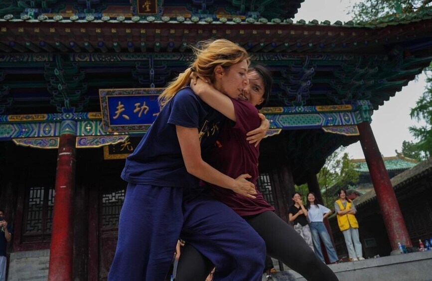 Two people embracing in front of a traditional Chinese pavilion with ornate decorations and a sign with Chinese characters. 2