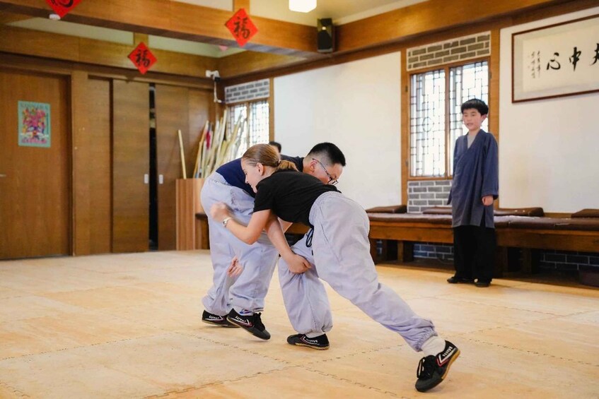 A martial arts training session with two participants in a traditional room with wooden floors and walls. 1