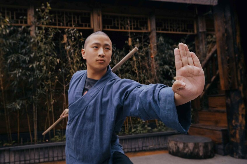 A person in traditional attire performing a martial arts stance outdoors. 5