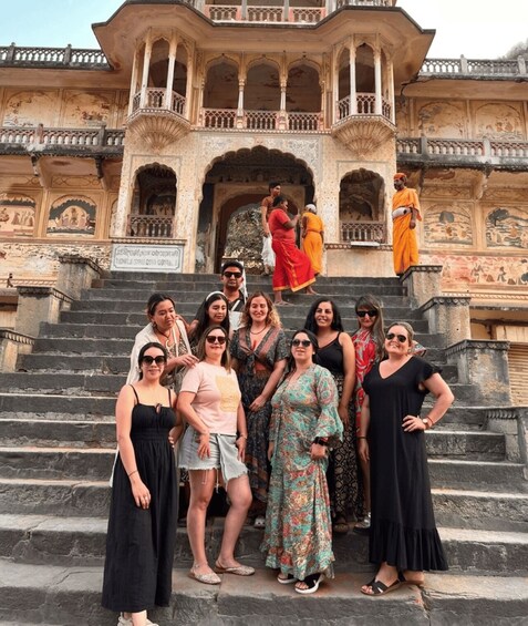 A group of people standing on stone steps in front of a historic building with intricate carvings and a balcony. 2
