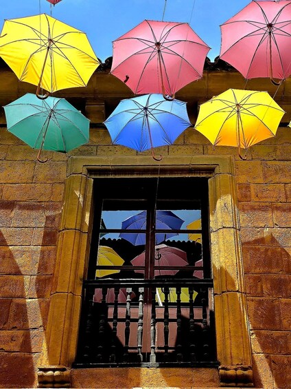 A building entrance with multiple colorful umbrellas hanging above. 1