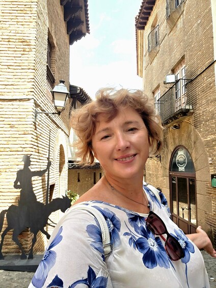 A person standing in a narrow street with brick buildings, a street lamp, and a horse statue. 3