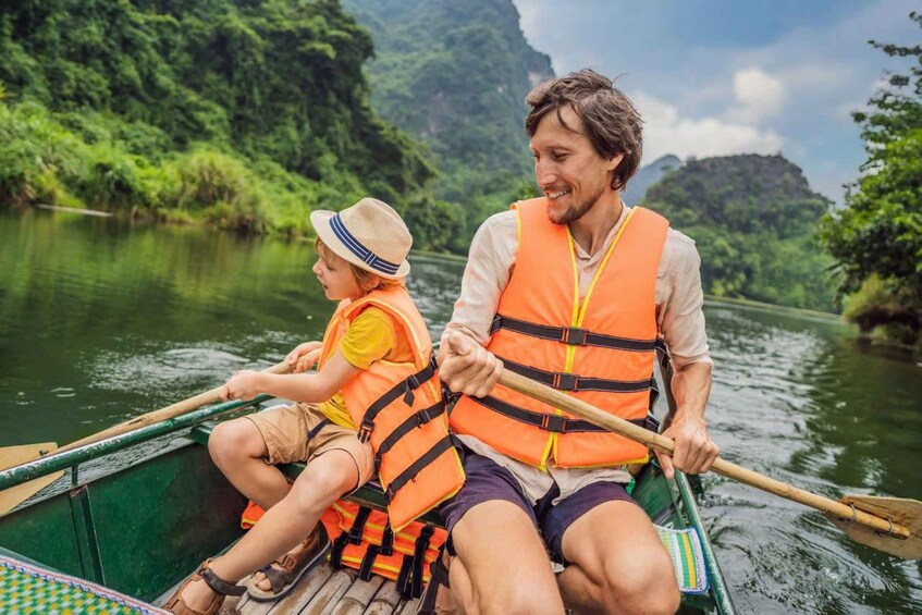 Two people in a green boat on a river, wearing orange life jackets. 1
