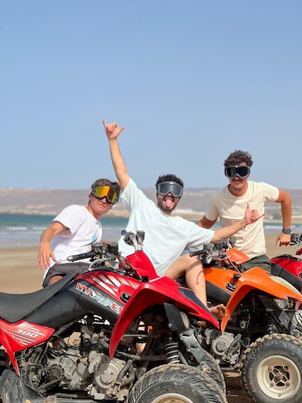 Three people on ATVs on a beach with the ocean in the background. 4