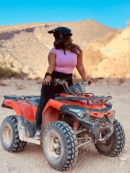 A person riding a red ATV in a desert landscape with rocky terrain and hills in the background. 5