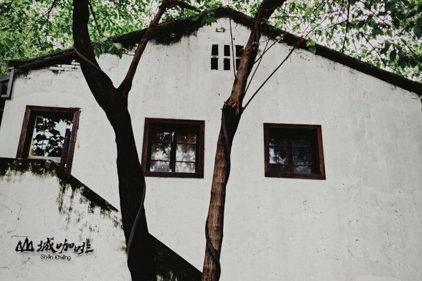 A white building with three windows and a tree in front. 4