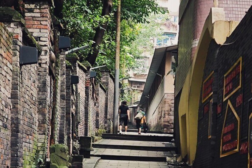A narrow alleyway with brick walls, a statue, and a staircase leading up. 1