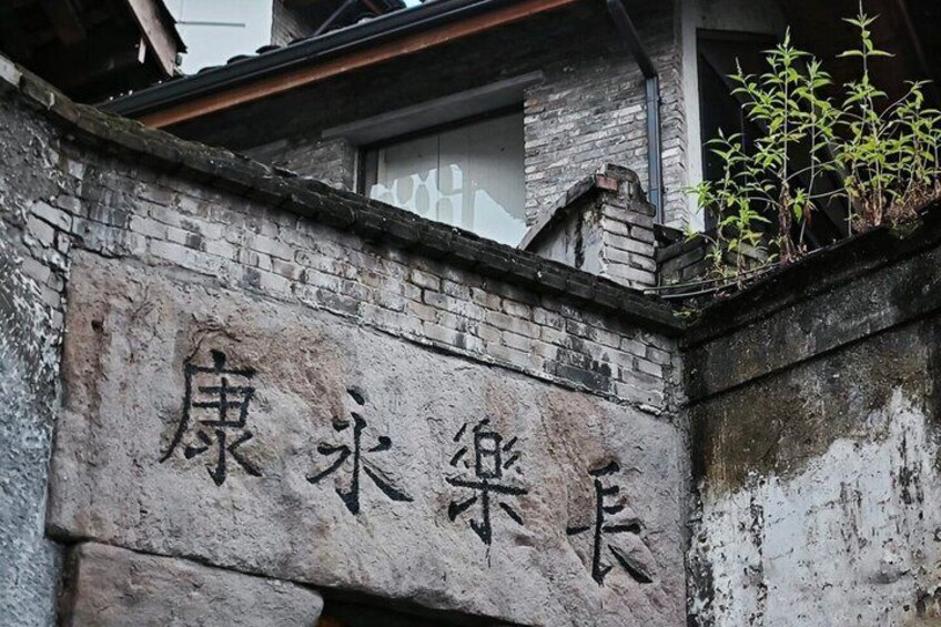 A weathered stone wall with Chinese characters and a small plant growing on top. 3