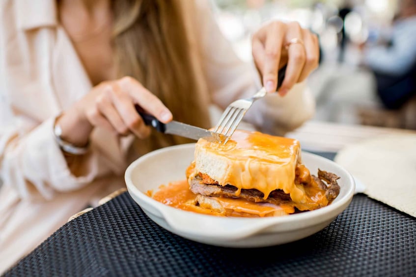 A person cutting a sandwich with melted cheese. 2