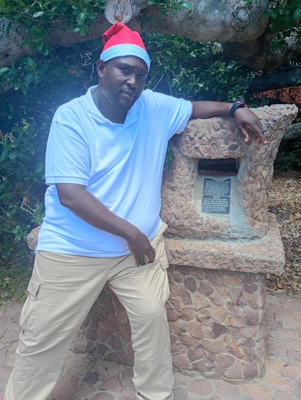 A man in a white shirt and beige pants leaning on a stone structure with a plaque. 3