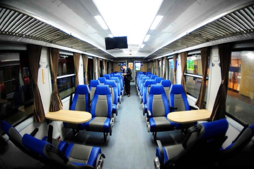 A train interior with blue and grey seats, a television screen, and a person walking down the aisle. 4
