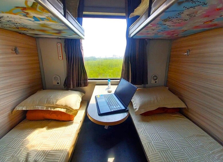A train compartment with two beds, a laptop on a table, and curtains. 5