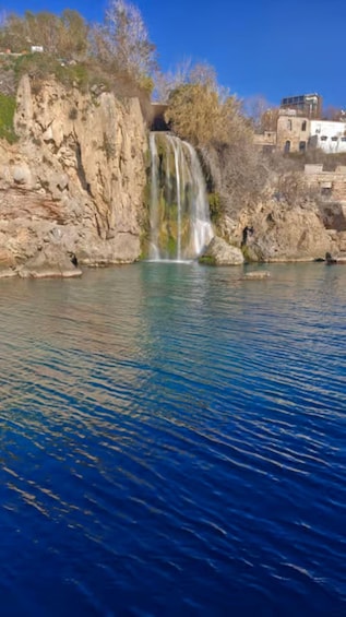A waterfall over a rocky cliff into a calm body of water, with buildings in the background. 4