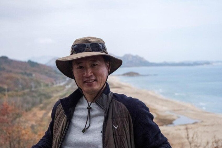 A person standing on a hill overlooking a beach with a mountainous backdrop. 2