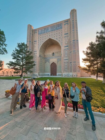 A group of people posing in front of a large, intricately designed building with a prominent archway. 3