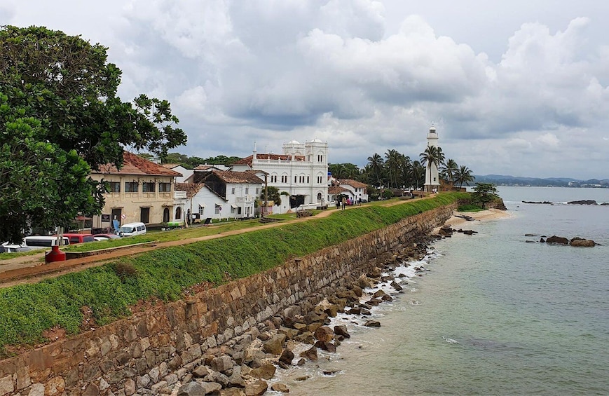 A coastal town with a stone seawall, white buildings, and a lighthouse. 3