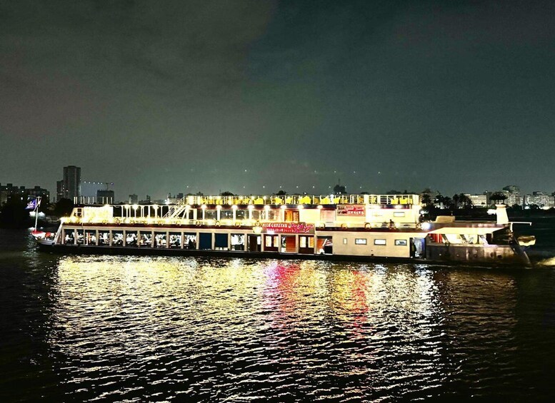 A riverboat with illuminated decks and a city skyline in the background. 1