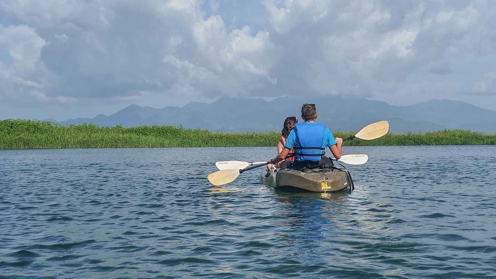 Two people kayaking on a calm lake with mountains in the background. 1