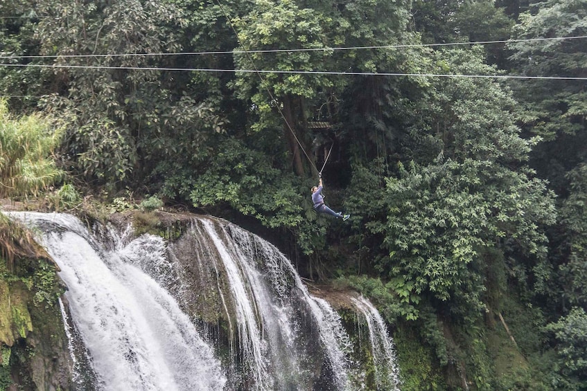A person zip-lining over a waterfall surrounded by dense forest. 4