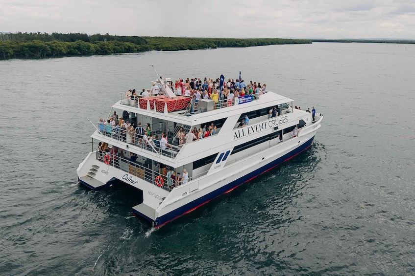 A large white cruise ship with 'ALL EVENT CRUISES' written on the side, named 'Calmar,' sailing on a body of water with a forested shoreline in the background. 3