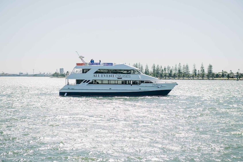 A large white cruise ship with 'ALL EVENT CRUISES' written on its side, sailing on a body of water with a clear sky and a line of trees in the background. 4