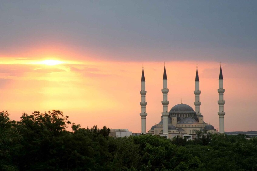 A mosque with four minarets and a dome, surrounded by trees, during sunset. 5