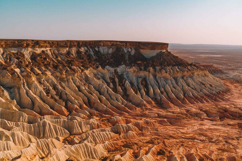 A vast, rugged terrain with layered rock formations and a flat horizon. 1