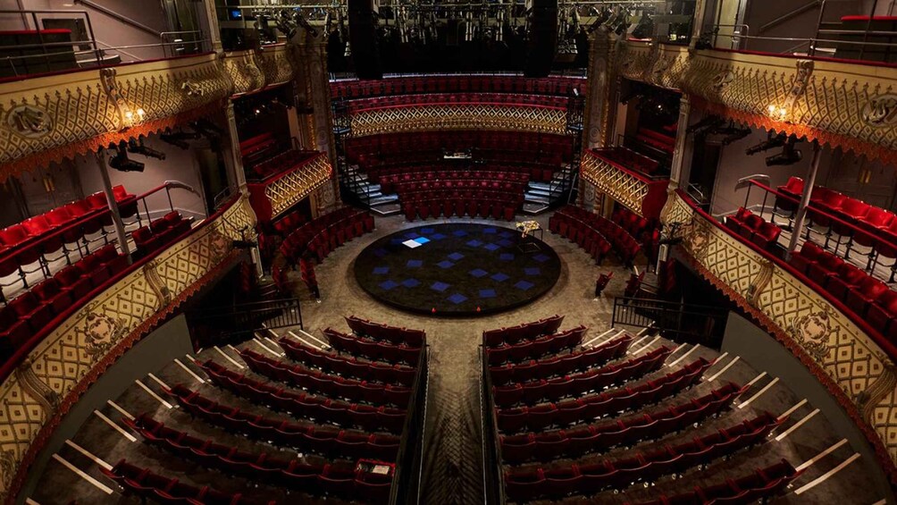 A grand theater with ornate golden railings, red velvet seats, and a central stage. 3