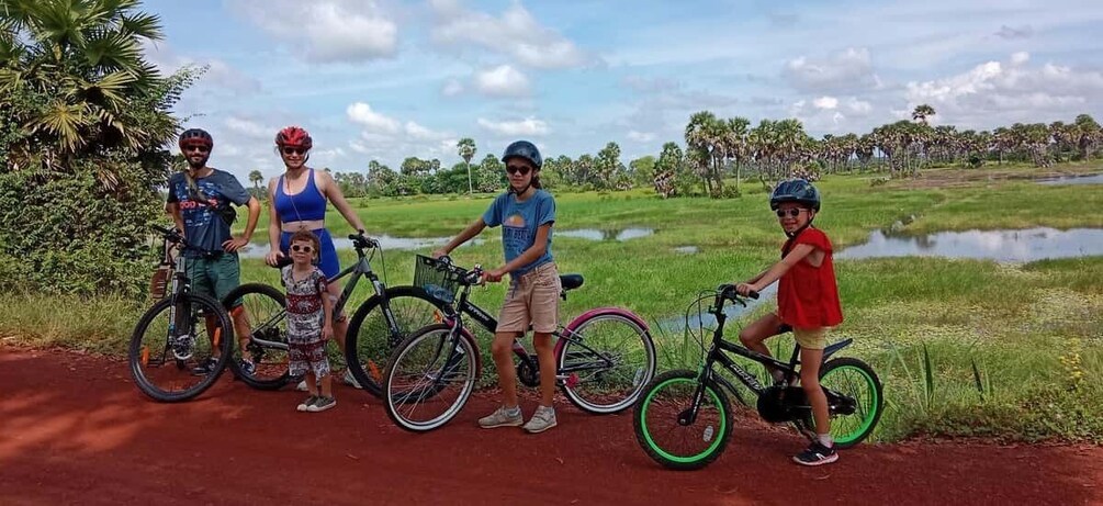 A group of people with bicycles on a dirt path near a water body, surrounded by greenery and trees. 4