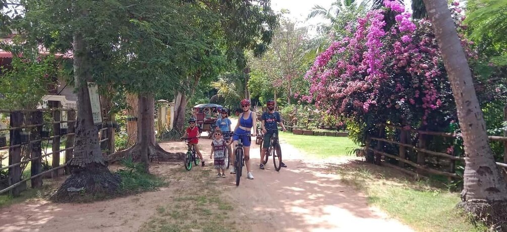 A dirt path with bicycles, people, and a pink flowering tree. 2