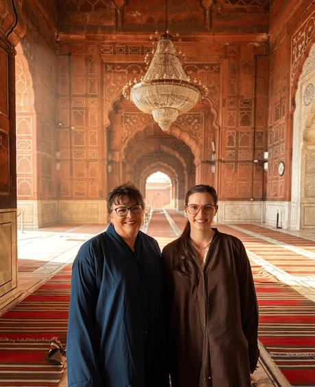 Two people standing in a historic building with intricate arches and a large chandelier. 3