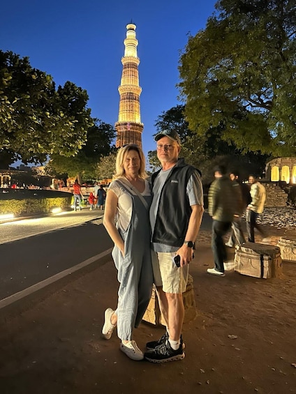 A couple standing in front of the illuminated Minaret of the Great Mosque, with trees and a paved area in the background. 5